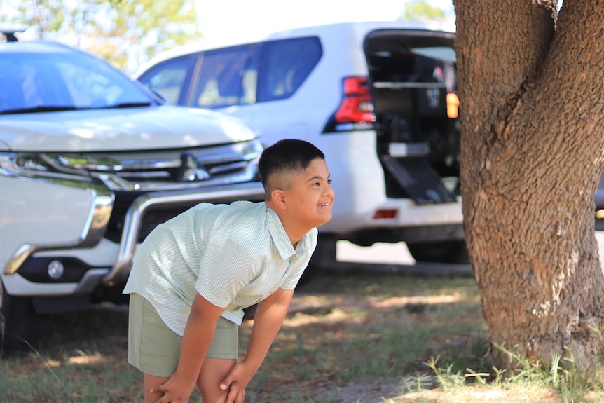 A young boy plays happily in front of a tree.