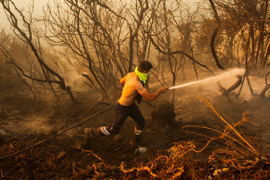 Man shirtless holds hoses up against orange blaze 