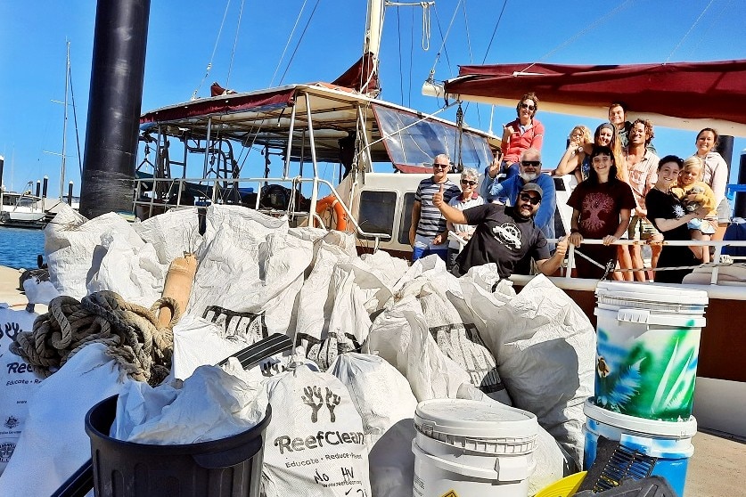 a group of people stand on a boat, with bags of rubbish in front of them. 