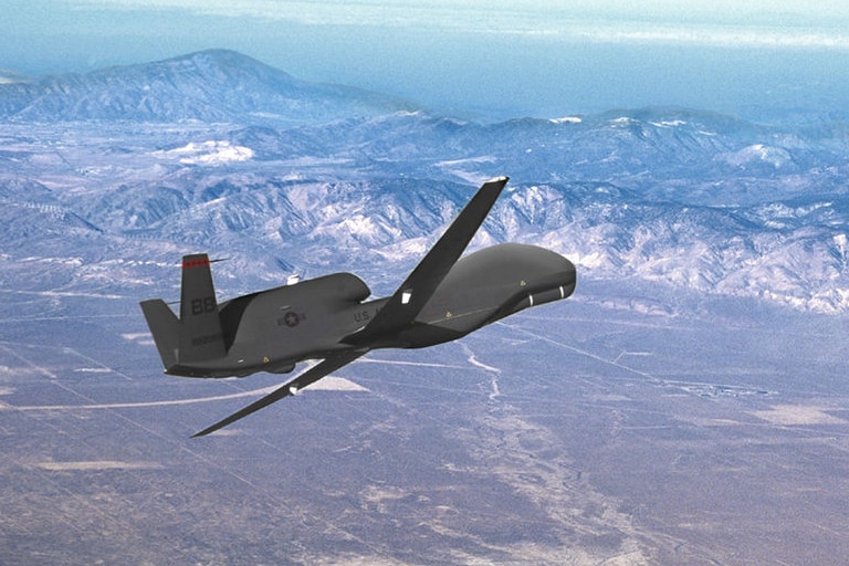 A Global Hawk drone made by Northrop Grumman flies above mountains.