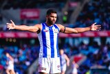 Tarryn Thomas in his North Melbourne jersey, standing with his arms outstretched on a field