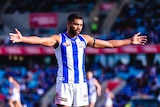 Tarryn Thomas in his North Melbourne jersey, standing with his arms outstretched on a field