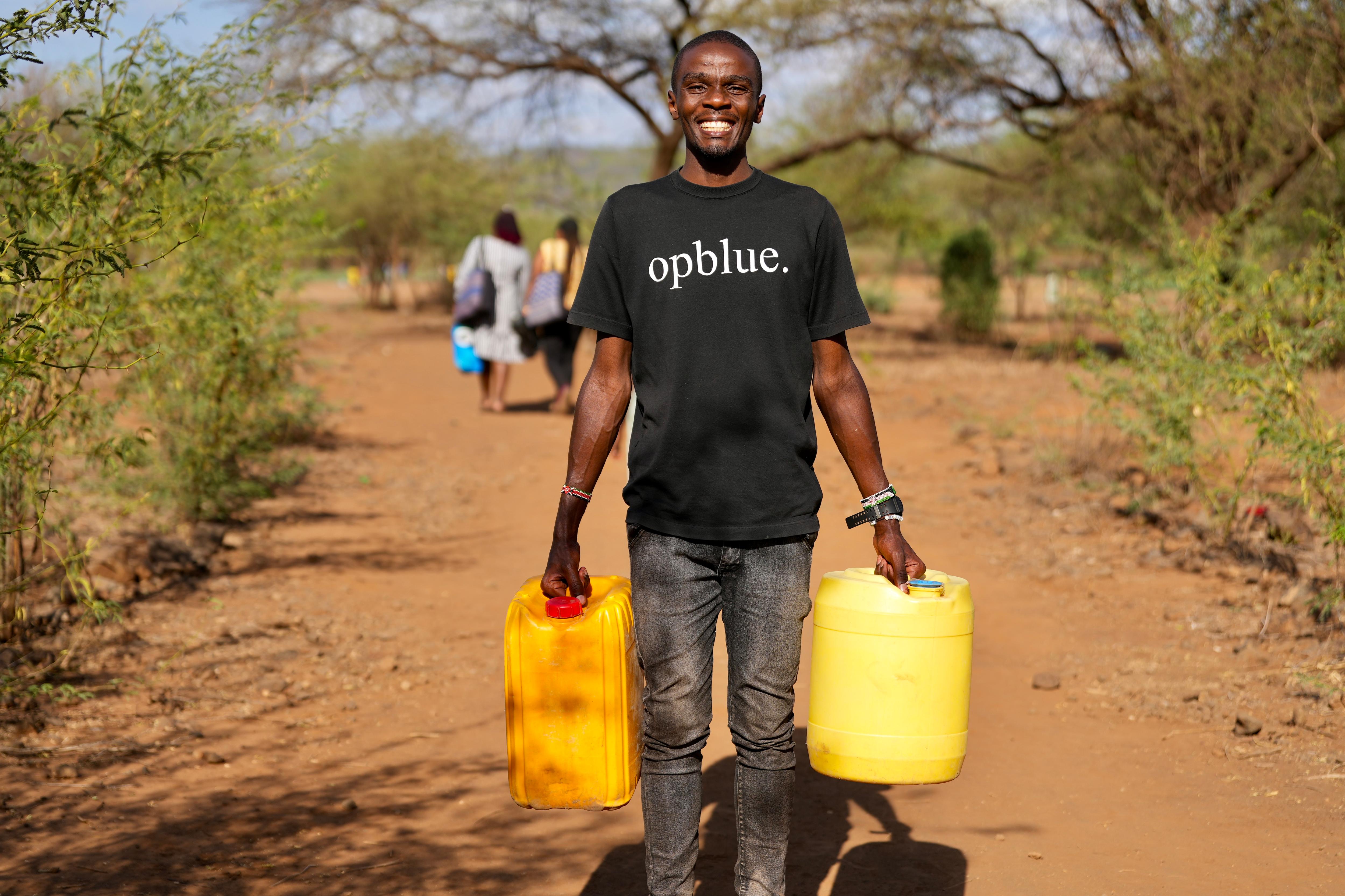 A man wearing an OpBlue t-shirt smiles and holds two plastic yellow water containers
