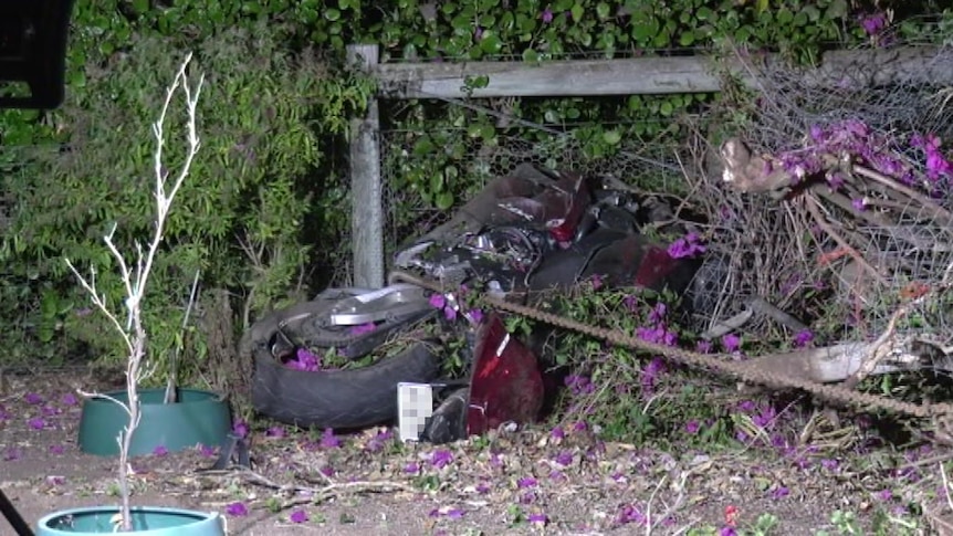 A motorcycle on its side against a fence after crashing.