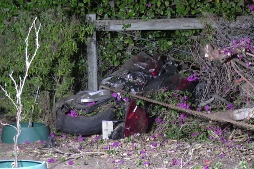 A motorcycle on its side against a fence after crashing.