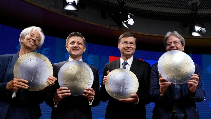 European finance leaders smile as they hold up big paper Euro coins.