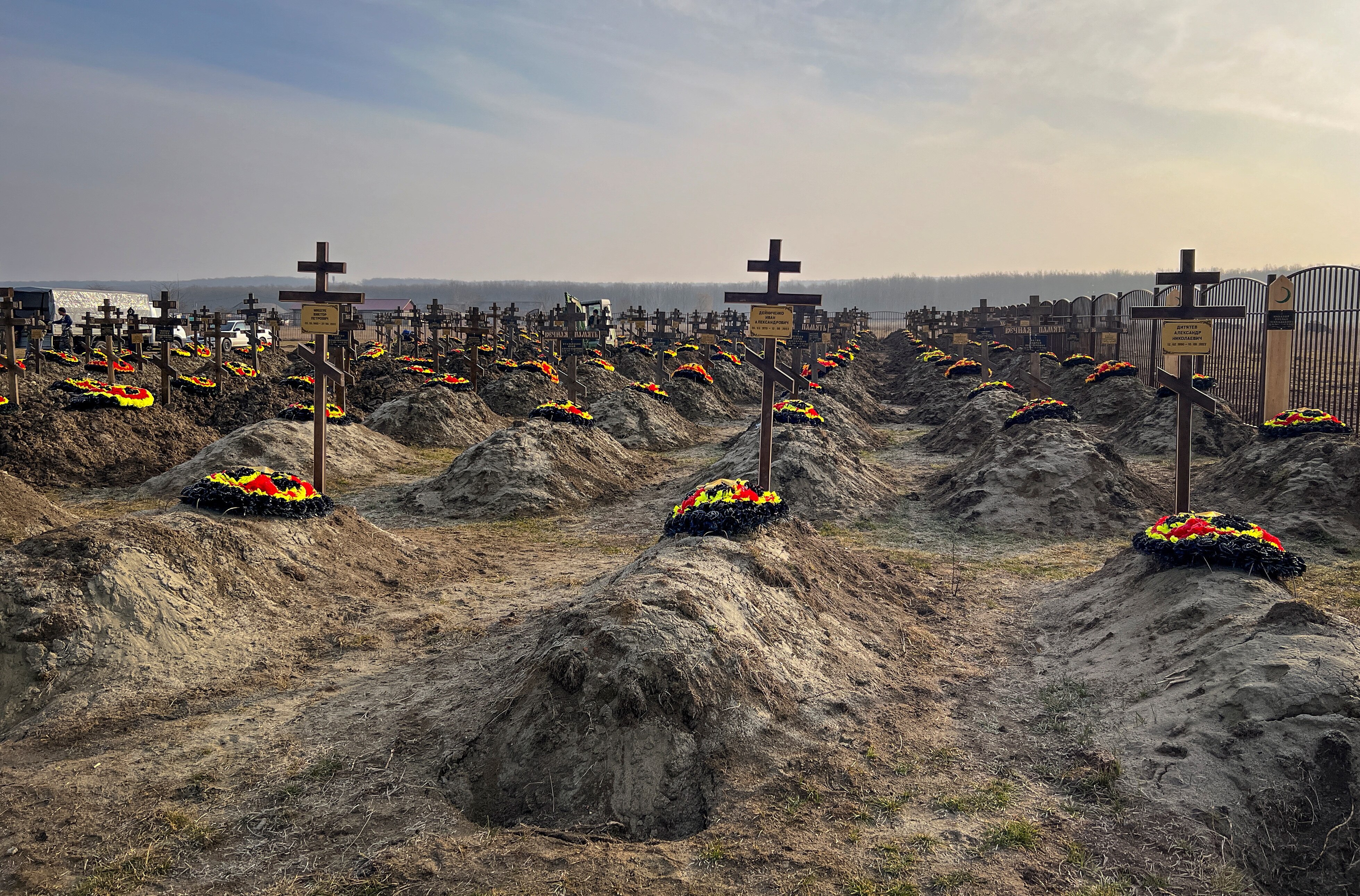 Dirt graves with wooden crosses and red, yellow and black wreaths. 