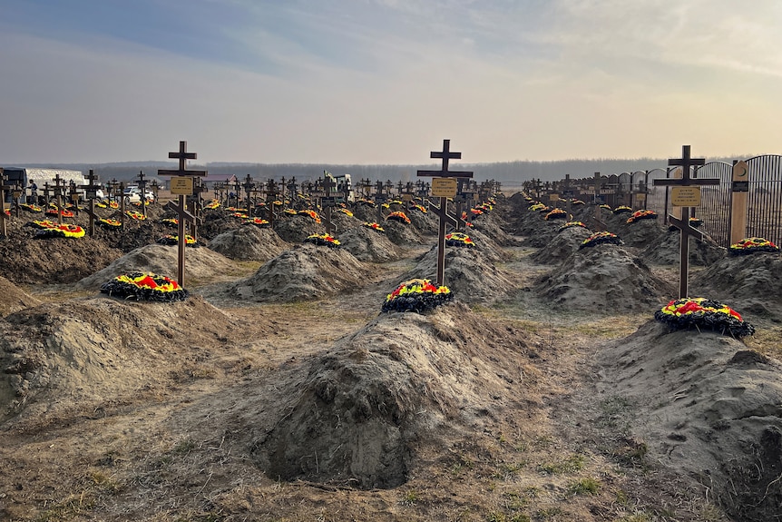 Dirt graves with wooden crosses and red, yellow and black wreaths. 