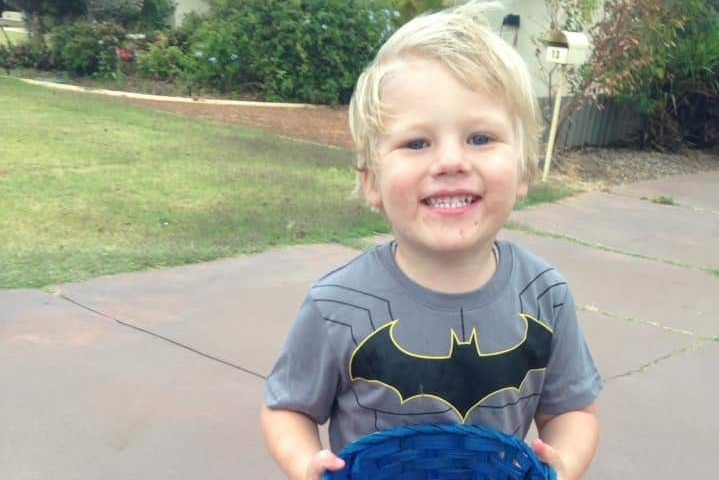 A little boy wearing a Batman T-shirt smiles and holds a basket of lollies.