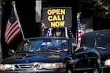 Protesters in a convertible car with a sign saying "open Cali now"