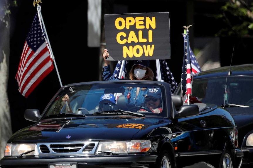 Protesters in a convertible car with a sign saying "open Cali now"