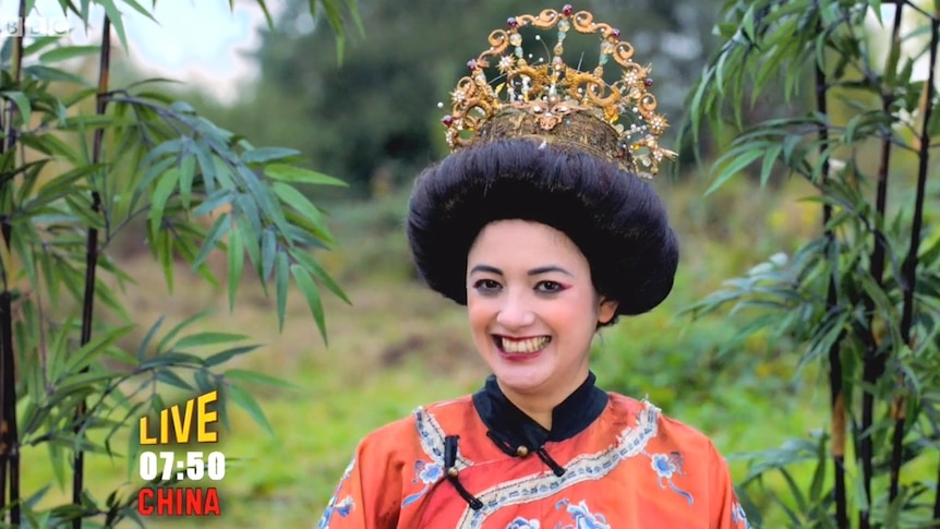 An actor in an ancient Chinese costumes smiles at the camera while on set standing among bamboo.