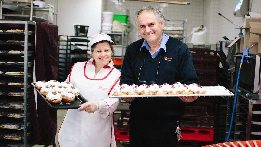 Couple and long-time employees Carmela and Santo holding freshly baked doughnuts