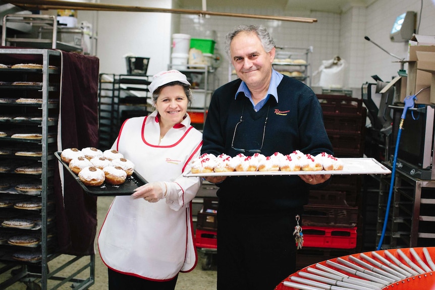 Couple and long-time employees Carmela and Santo holding freshly baked doughnuts