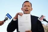 Tony Abbott holds up a piece of paper while speaking to the press.