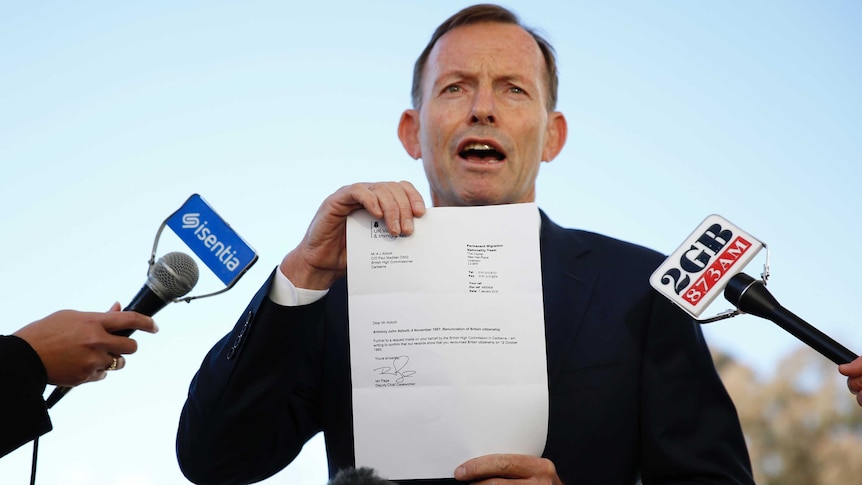 Tony Abbott holds up a piece of paper while speaking to the press.