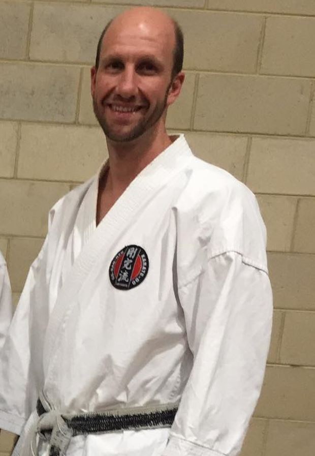 A man wearing a karate uniform smiles.
