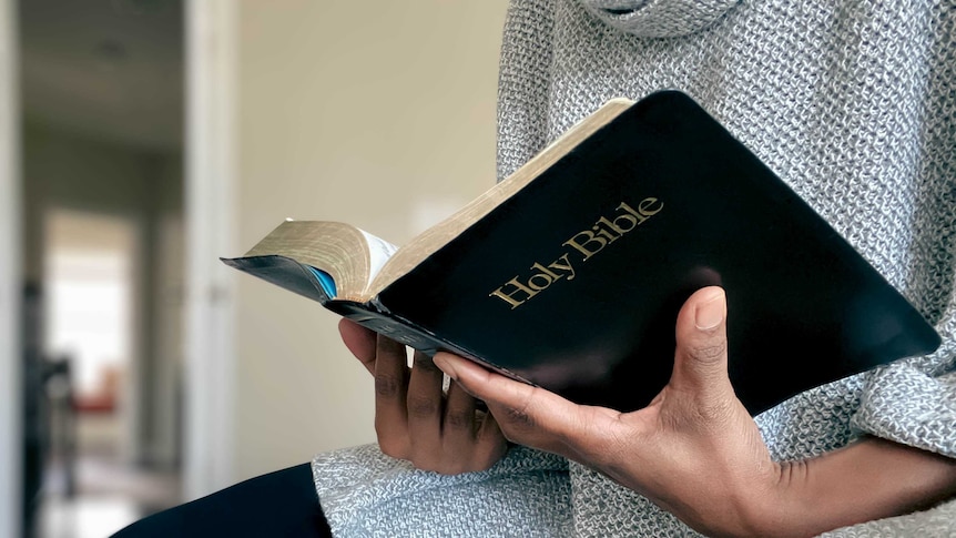 woman holds Bible open in her hands in house setting