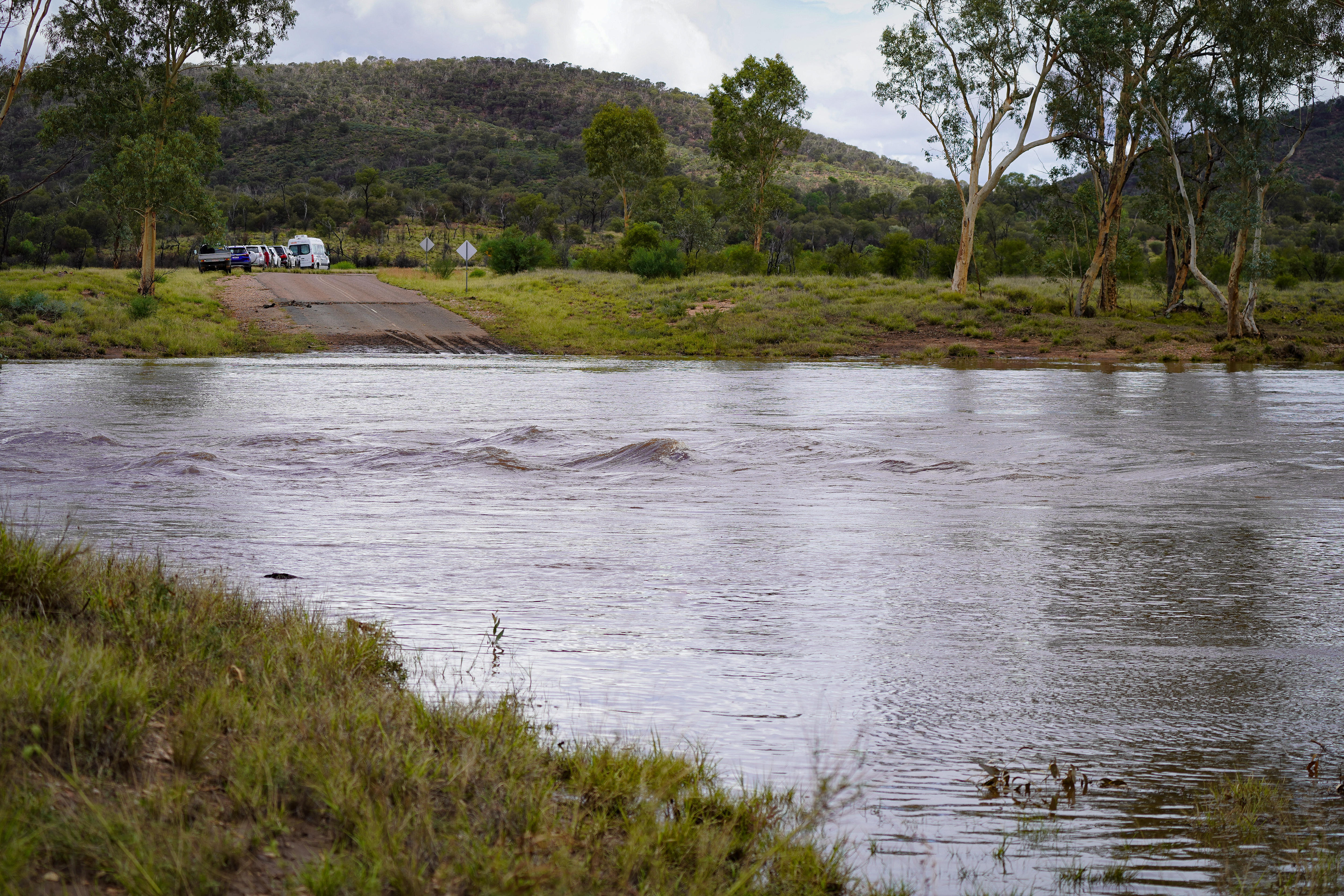 Vista de un río crecido que ha inundado una carretera mientras los vehículos están varados al otro lado del agua.