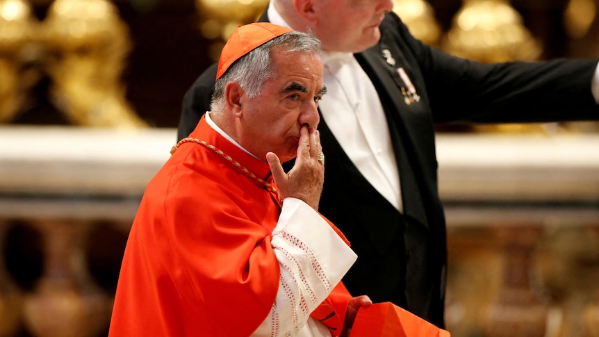 Cardinal wearing red robes holds hand to his face