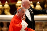 Cardinal wearing red robes holds hand to his face