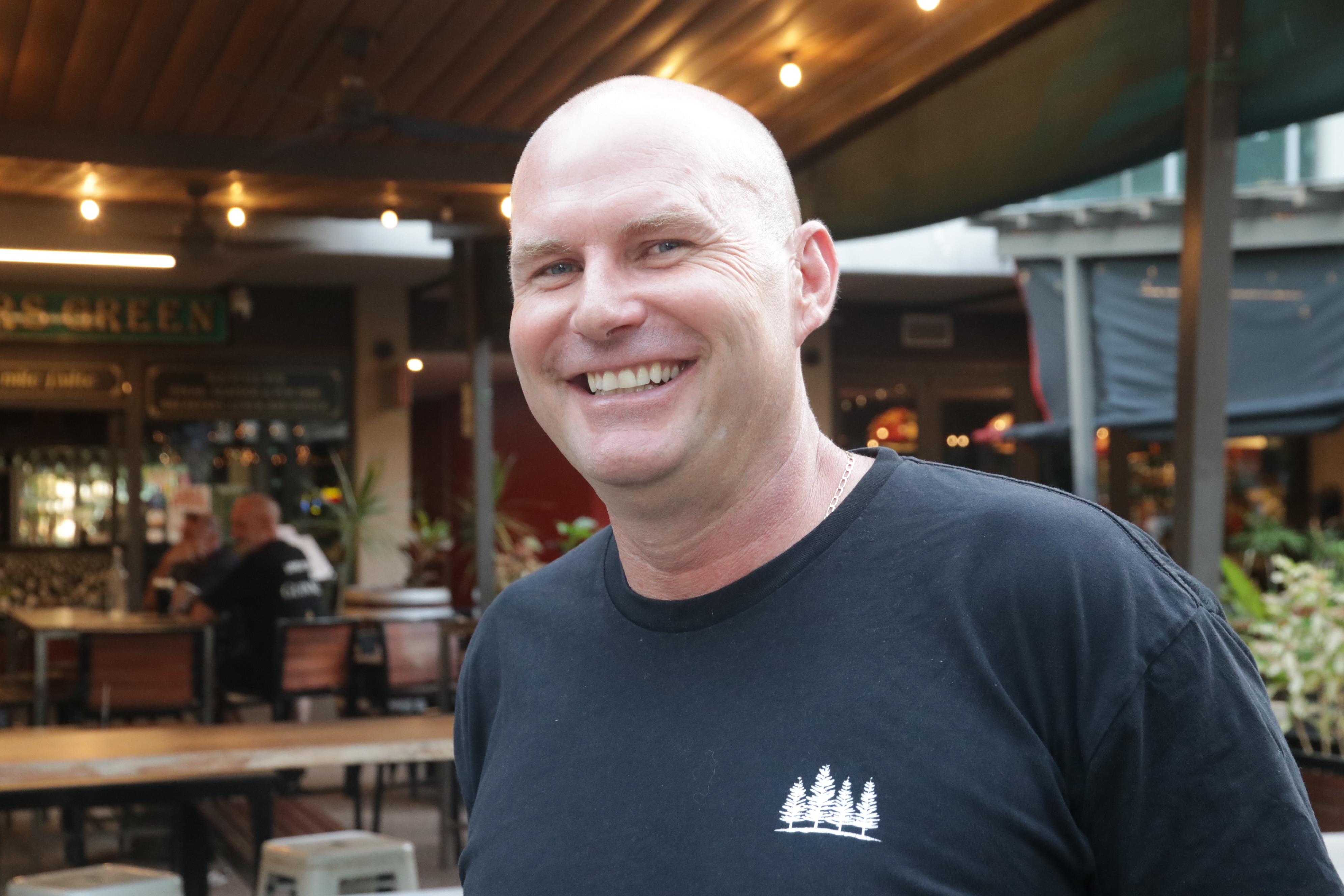 A bald man in a black t-shirt smiles