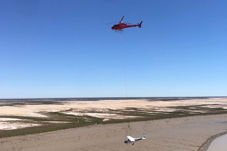 A red helicopter flying a white aeroplane through a muddy Kimberley landscape