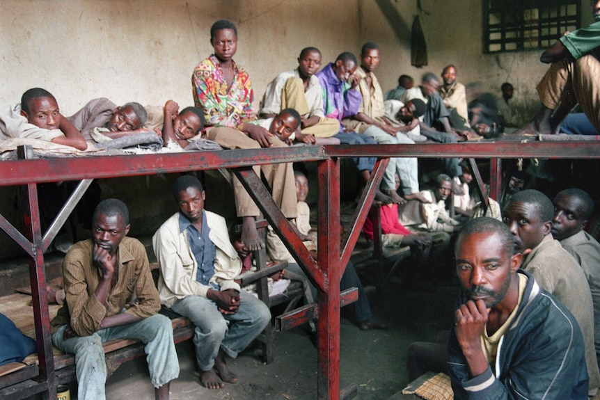 A dozen men accused of war crimes sit on bunks