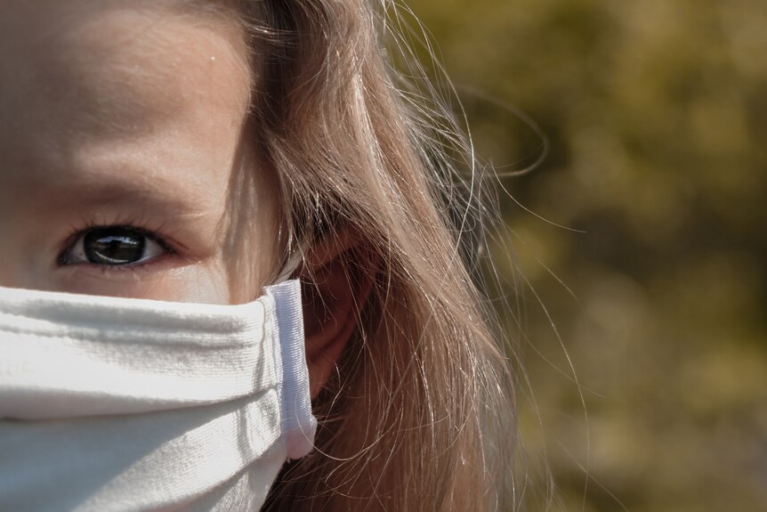Unidentified girl wears face mask in outdoor setting.