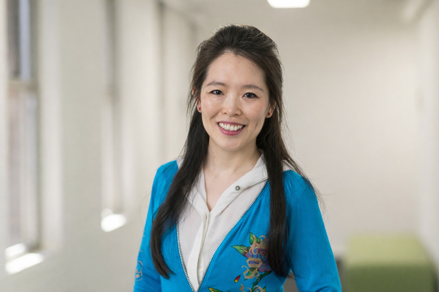 A smiling, dark-haired woman in a corridor.