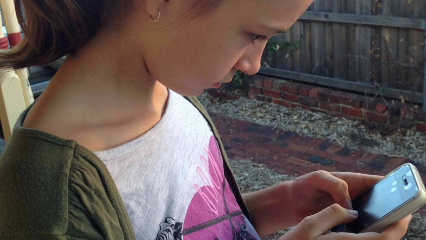 A young girl stares at a mobile phone screen.