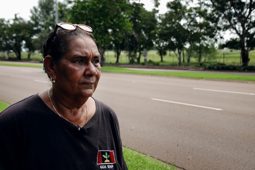 an aboriginal woman looking at a road with trees in the background