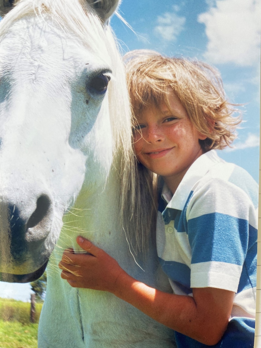 Young girl with head leaning against white horse.