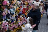 A woman and child look at flowers and photos of victims of war on a memorial