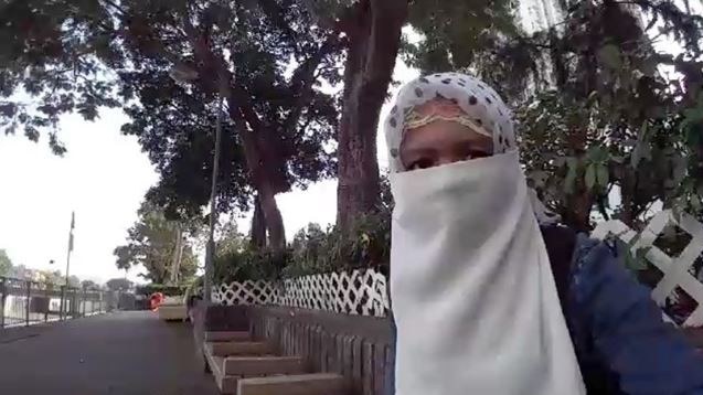 An Indonesian woman wearing a Niqab sits on a park bench.