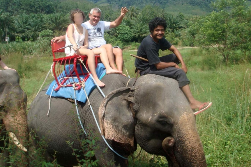 Oleg Kouzmine sits on the back of an elephant with a girl.