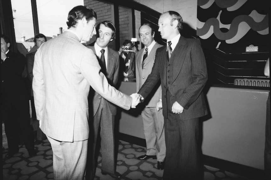 Prince Charles is seen shaking hands with someone. Harry M Miller is to his left.