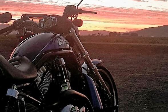A Harley Davidson motorbike in an open area and an orange sunset.
