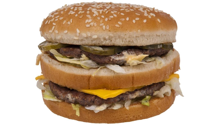 A hamburger with a sesame seed bun, two meat patties, pickles, cheese and white sauce