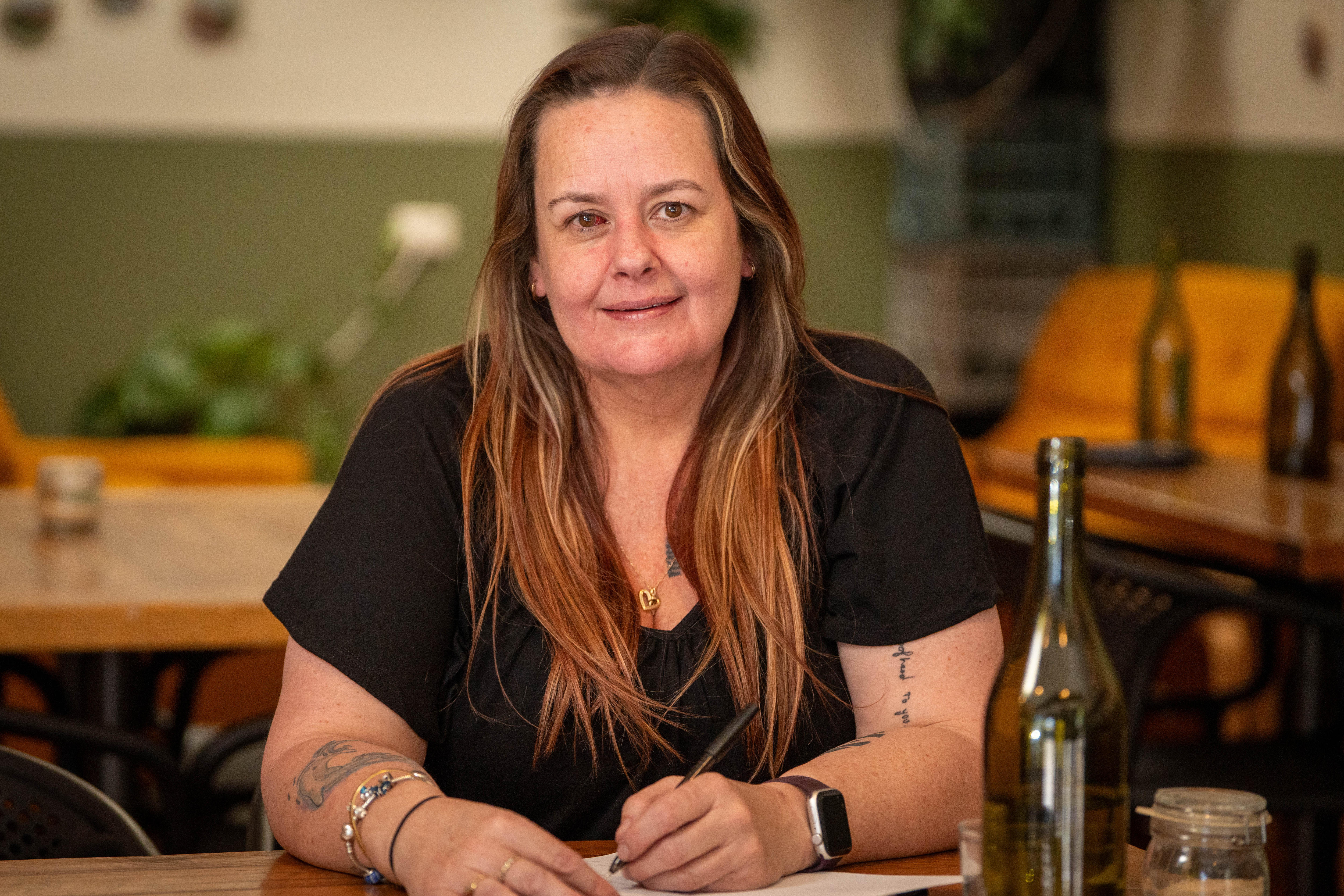 Una mujer con el pelo largo sonríe a la cámara mientras está sentada en un café