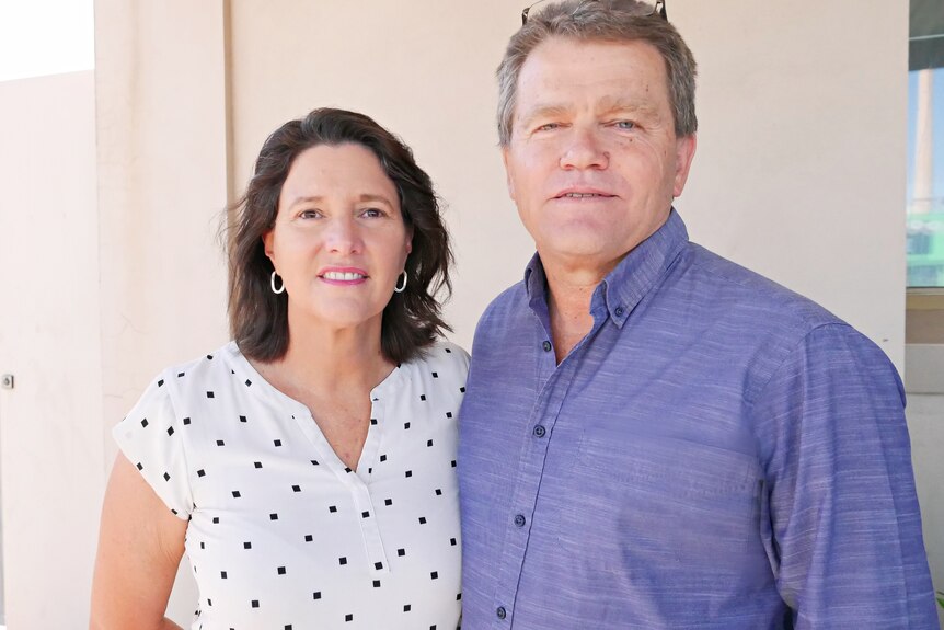 A woman wearing a polka dot shirt and a man in a blue shirt, in their 50s pose for a photo