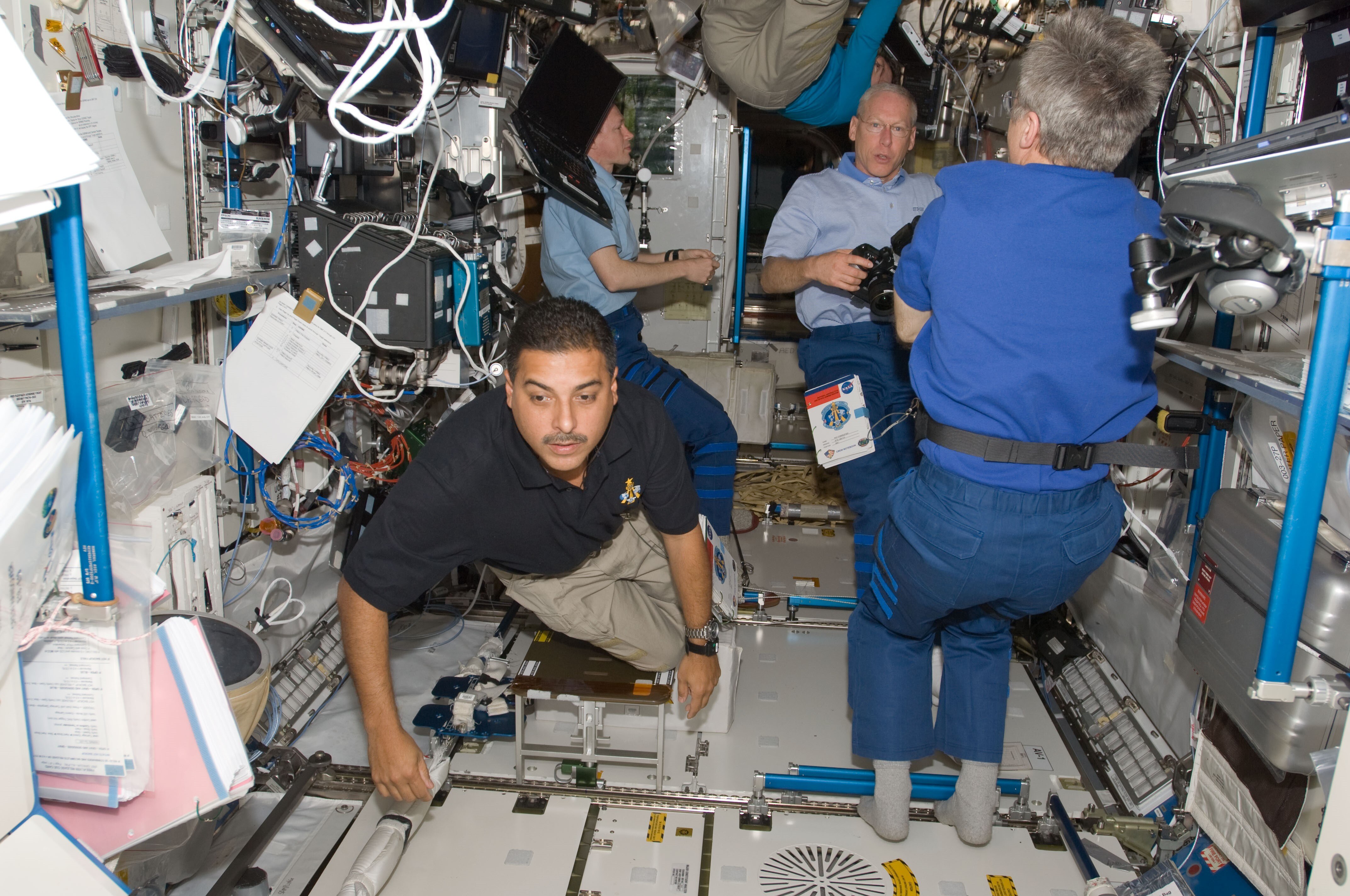 Jose Hernandez floats in a space capsule next to two sitting astronauts
