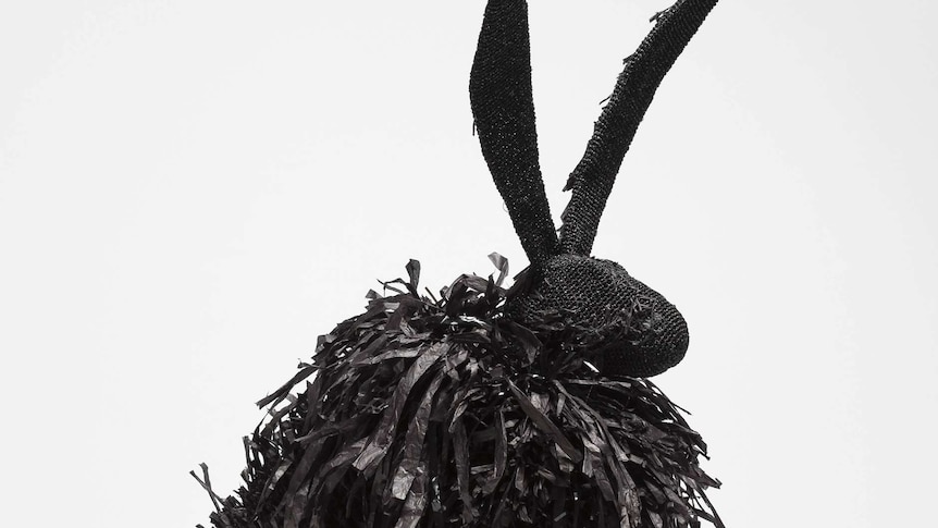 A sculpture of a black hare with crocheted skin and a mane of scruffy hair.