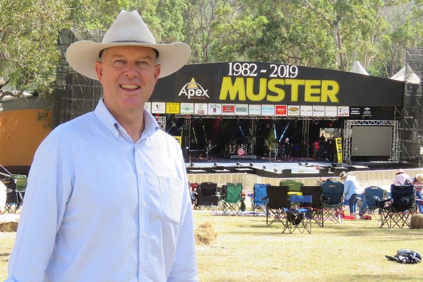 A man in a long-sleeved collared shirt and wide-brimmed hat stands in front of the muster stage.