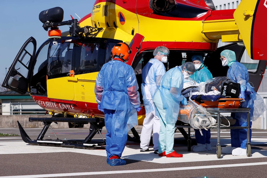 A group of health workers surrounding a patient on a stretcher next to a helicopter