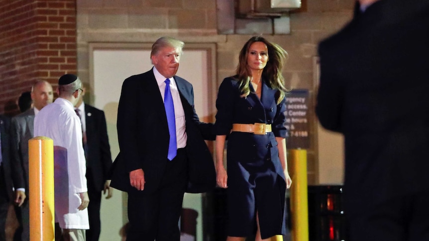 Donald Trump puts his hand on Melania Trump's back as they walk towards their car after visiting the hospital.