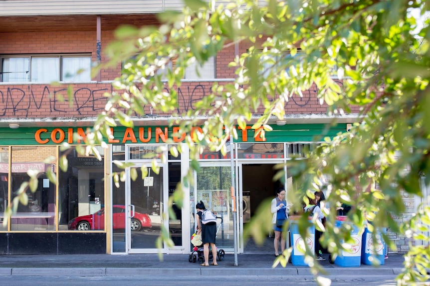 Layla attends to her daughter, who is sitting in a stroller, standing outside a laundromat.