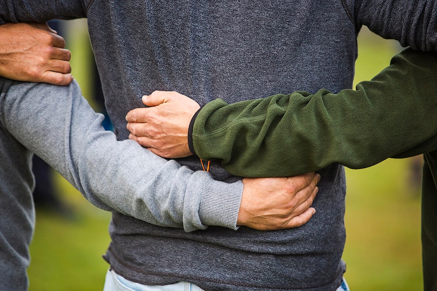 Colour photo of men with their arms around each other's backs.