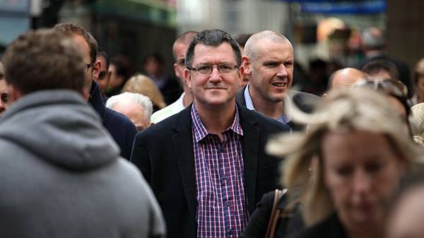 Financial adviser David French poses amid a bustling city street, surrounded by people.