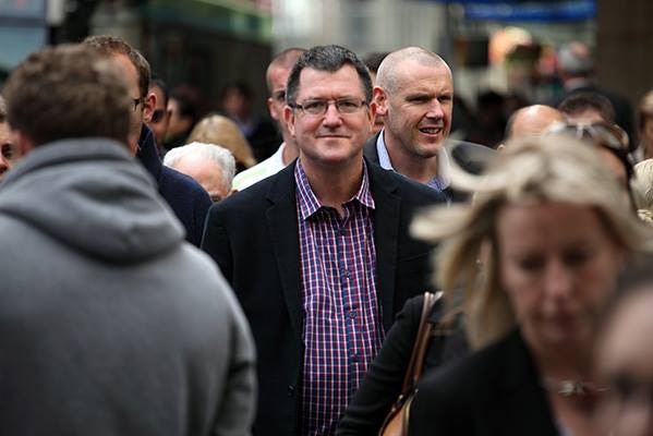 Financial adviser David French poses amid a bustling city street, surrounded by people.